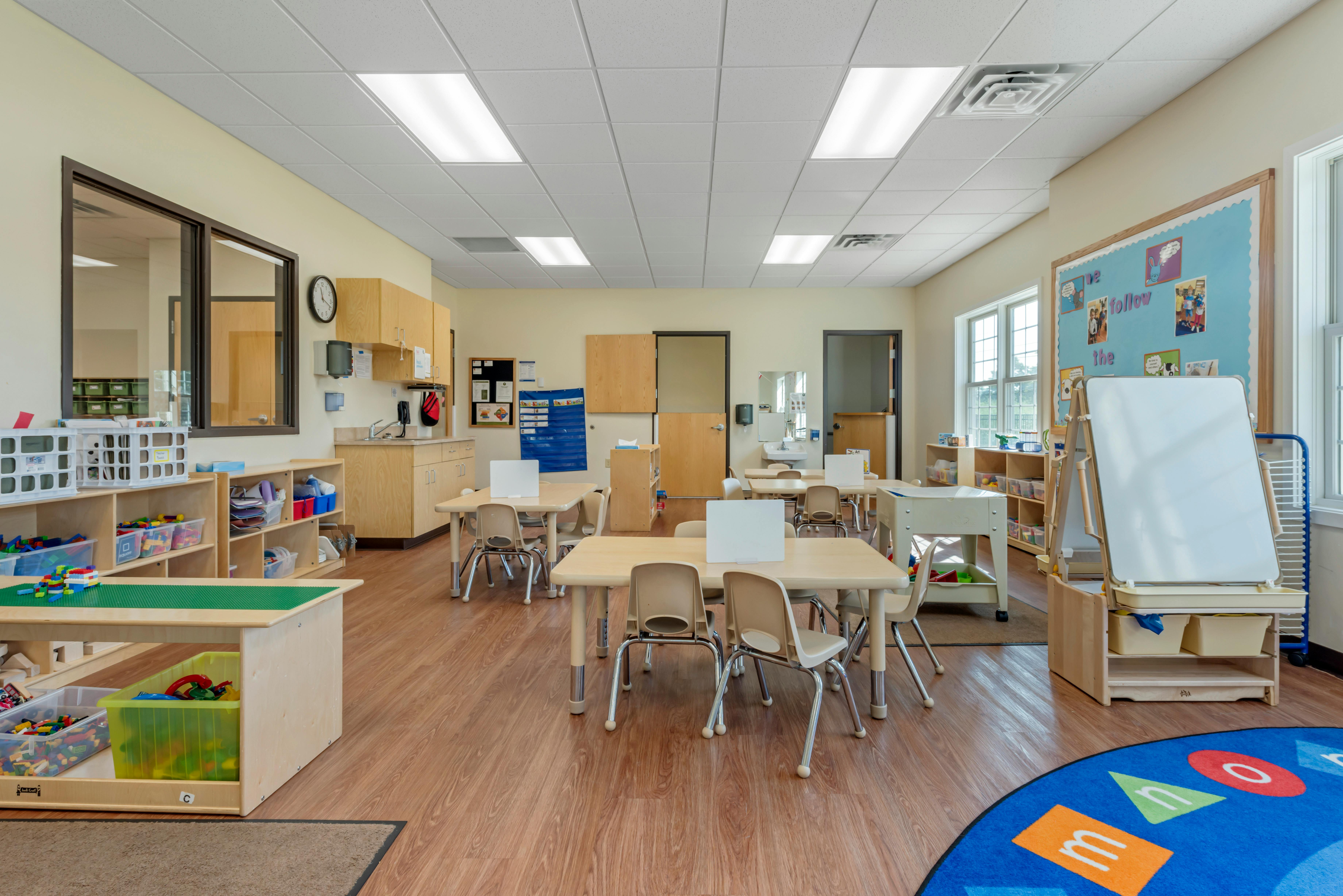 Empty classroom with small tables and chairs, shelves with toys and supplies