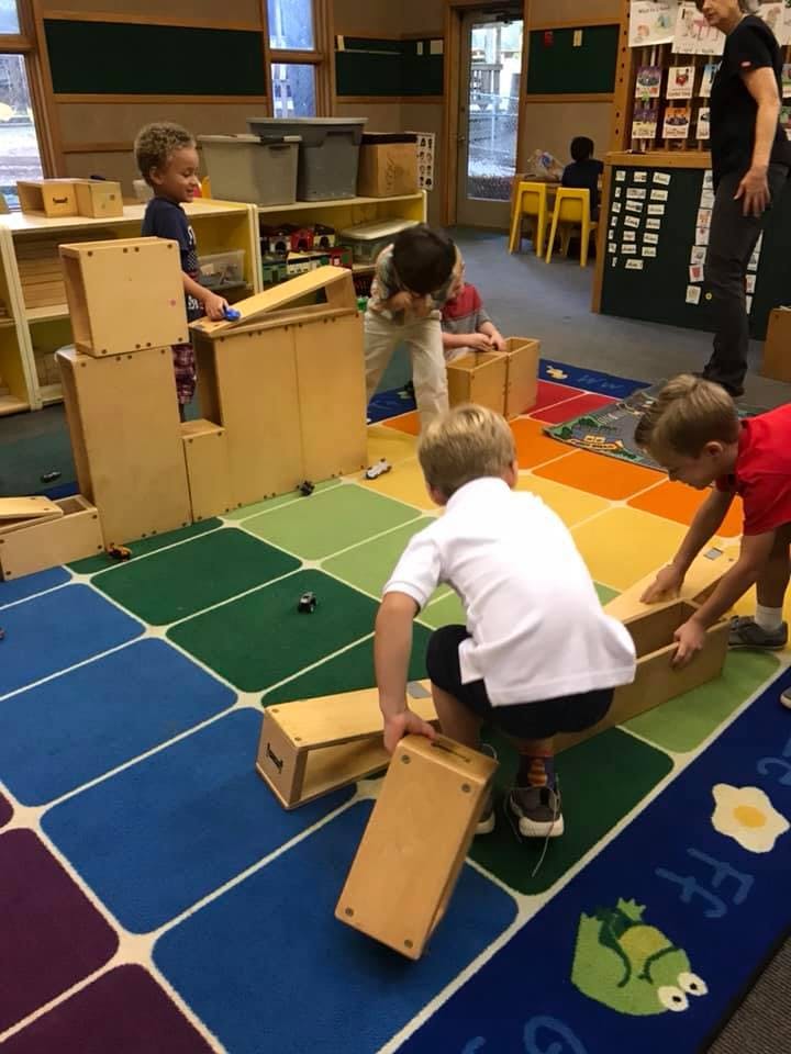 Children playing with wooden blocks on a colorful rug in a classroom