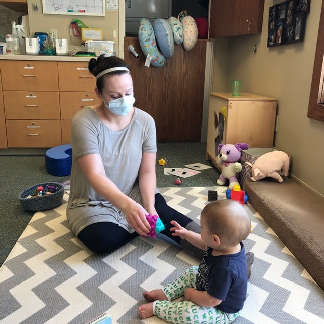 Person in mask playing with a child on a mat