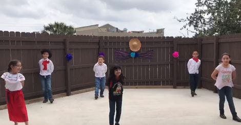 Five children standing in an outdoor area with a wooden fence