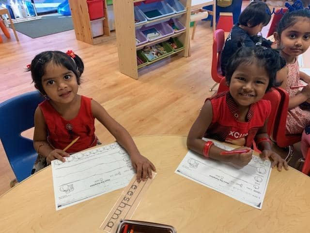 Two children sitting at a table with papers and writing utensils