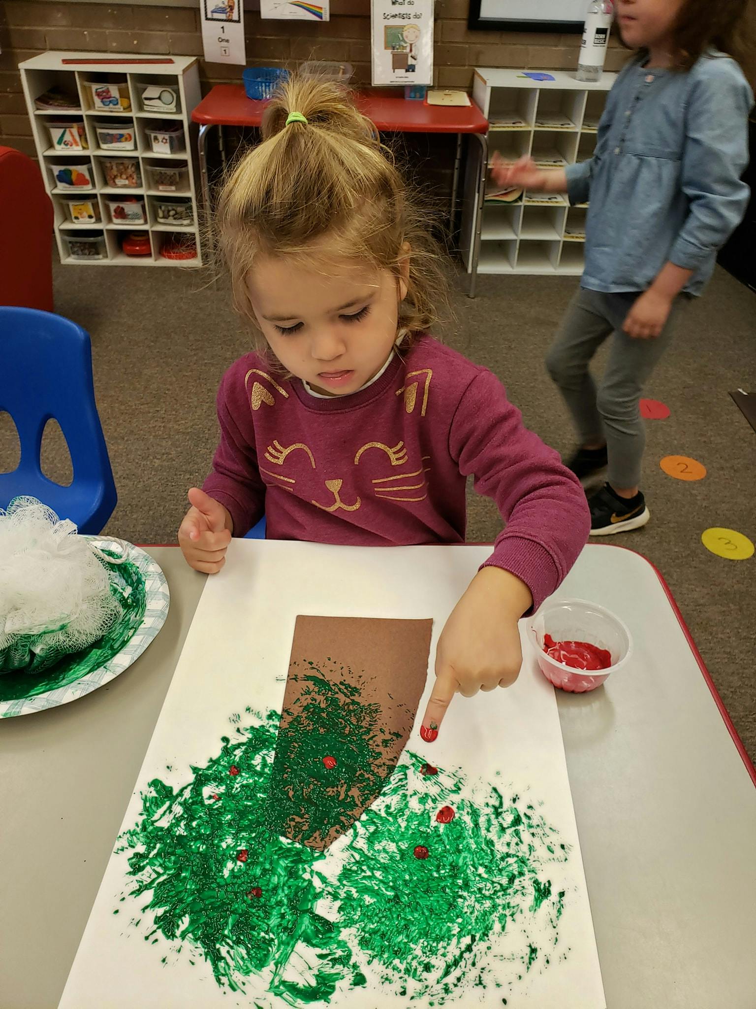 Child finger painting green and red on a paper tree