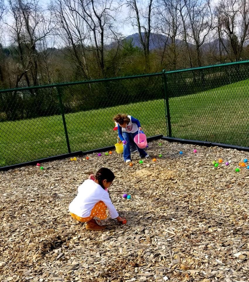Two children collecting colorful objects from wood chips