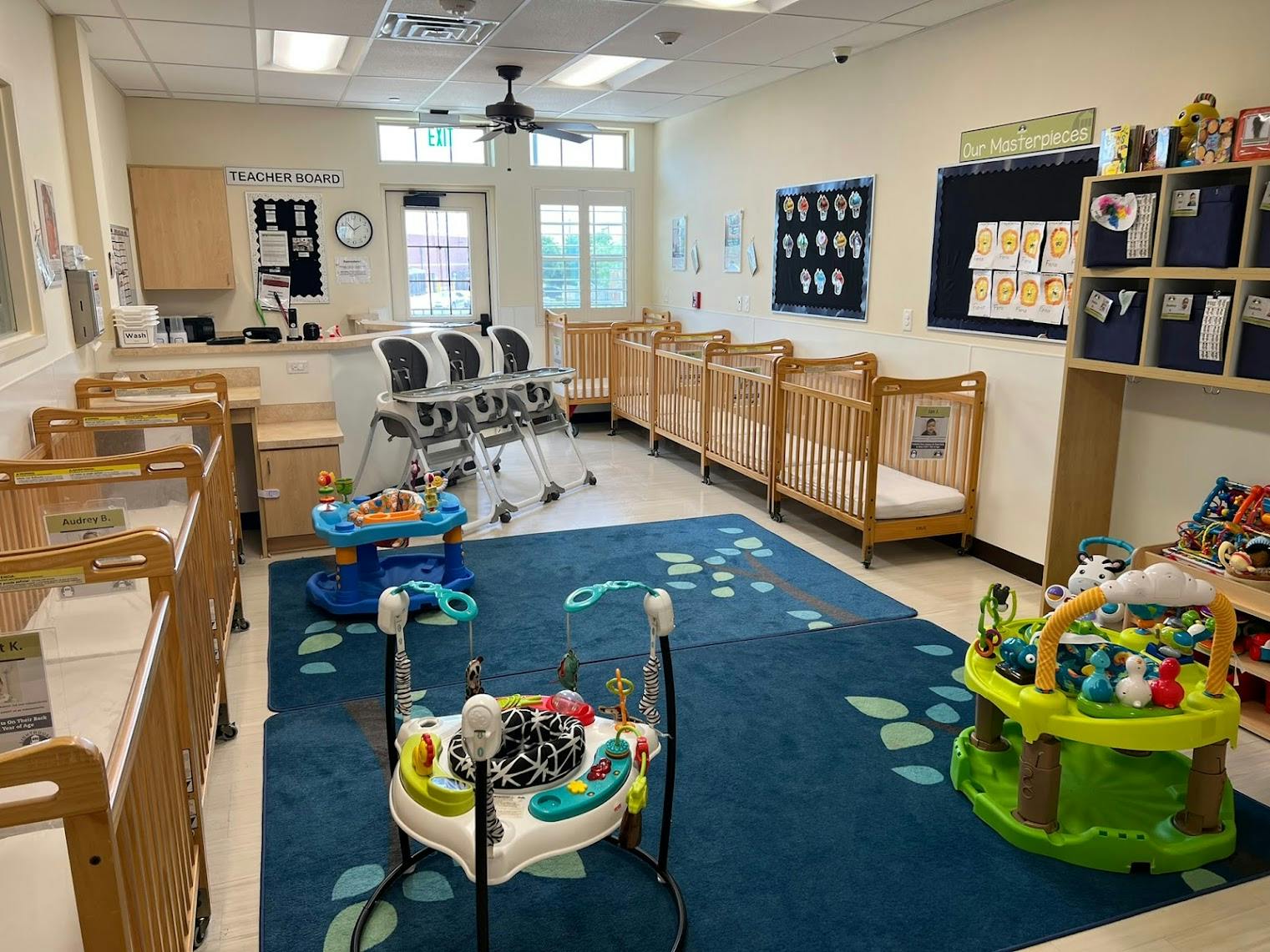 Empty infant daycare room with cribs, high chairs, and baby activity centers