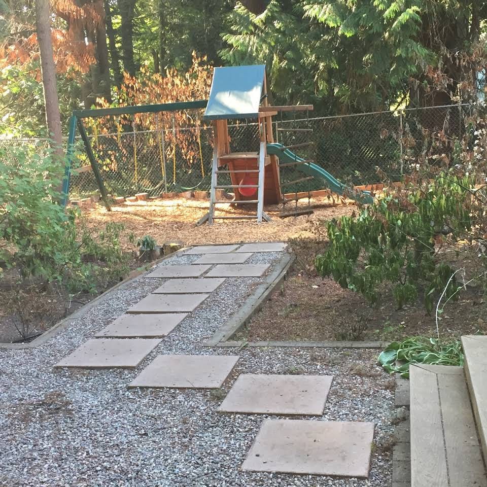 Playground with swings and slide behind a gravel path with stepping stones