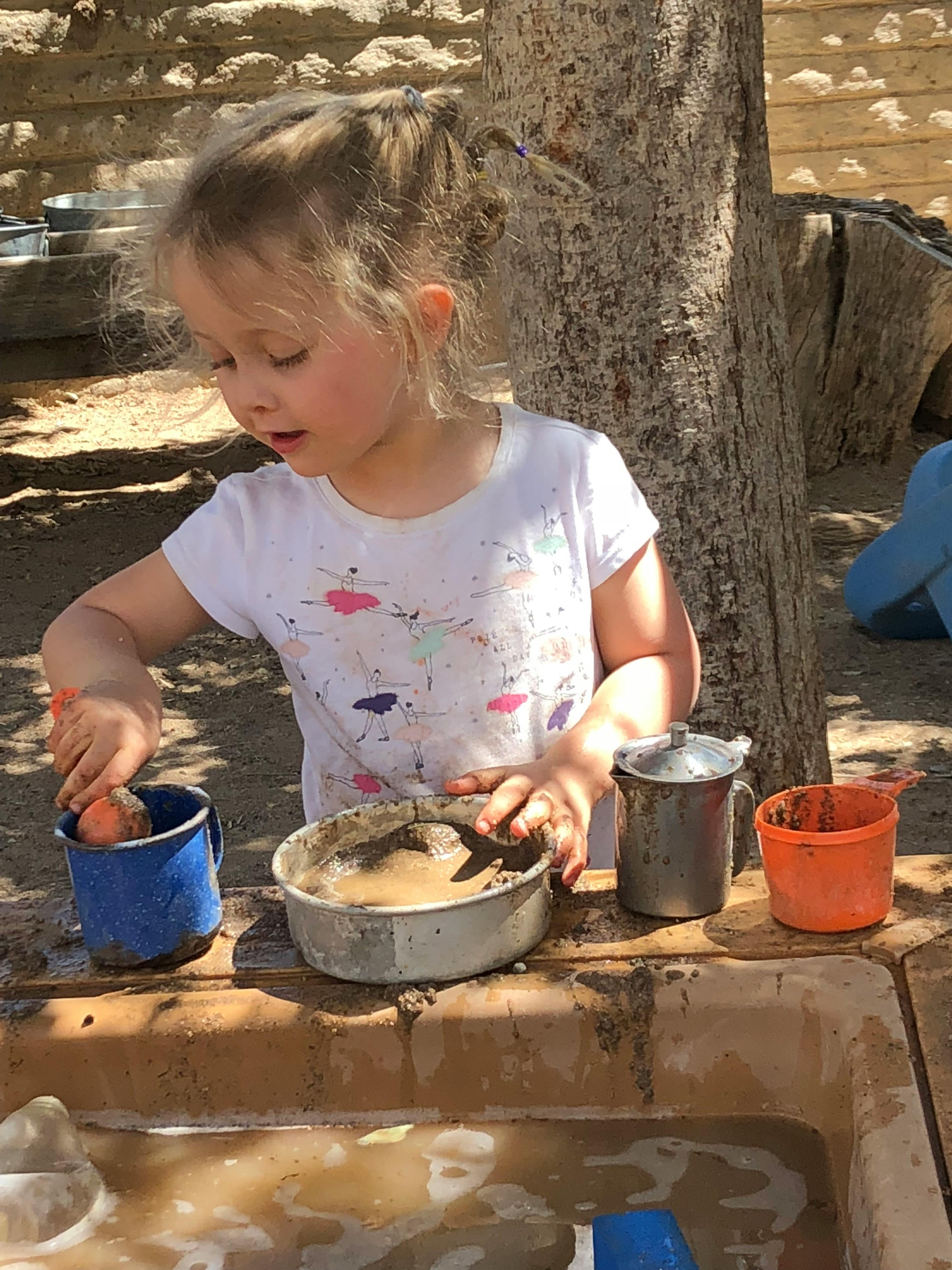Child playing with mud and containers outdoors with containers