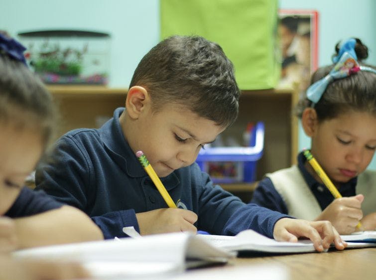 Children writing in notebooks at desks in a classroom