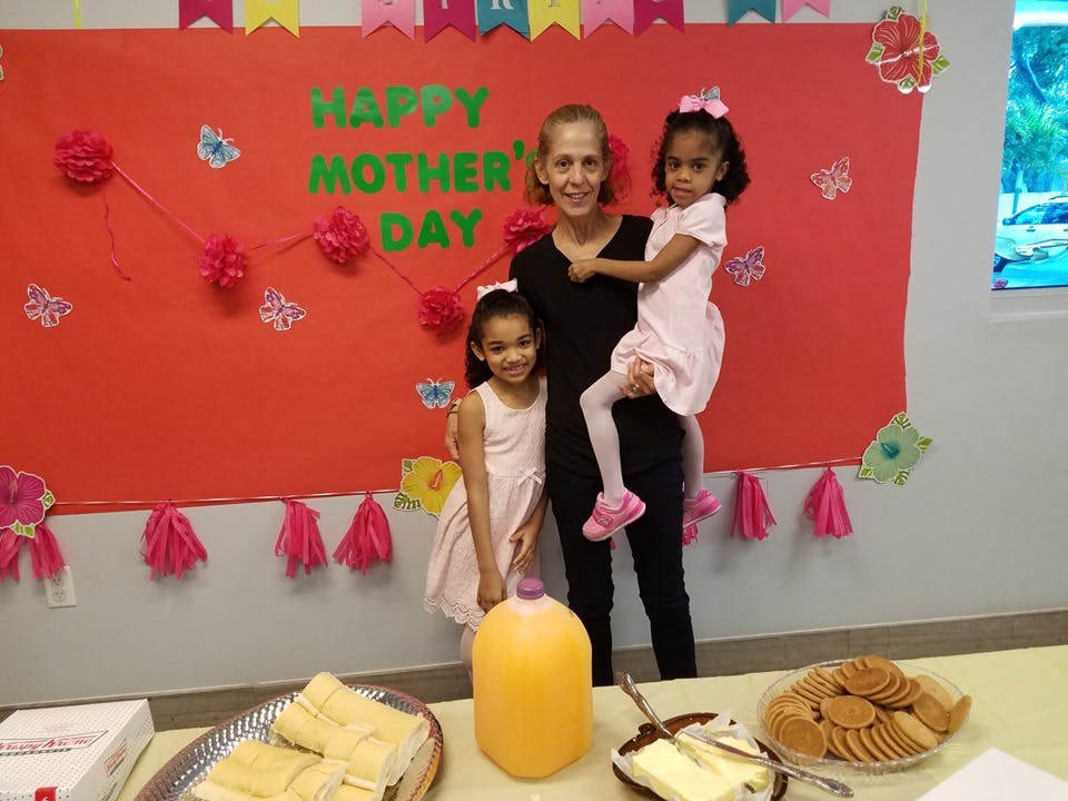 Adult and two children standing in front of a "Happy Mother's Day" sign