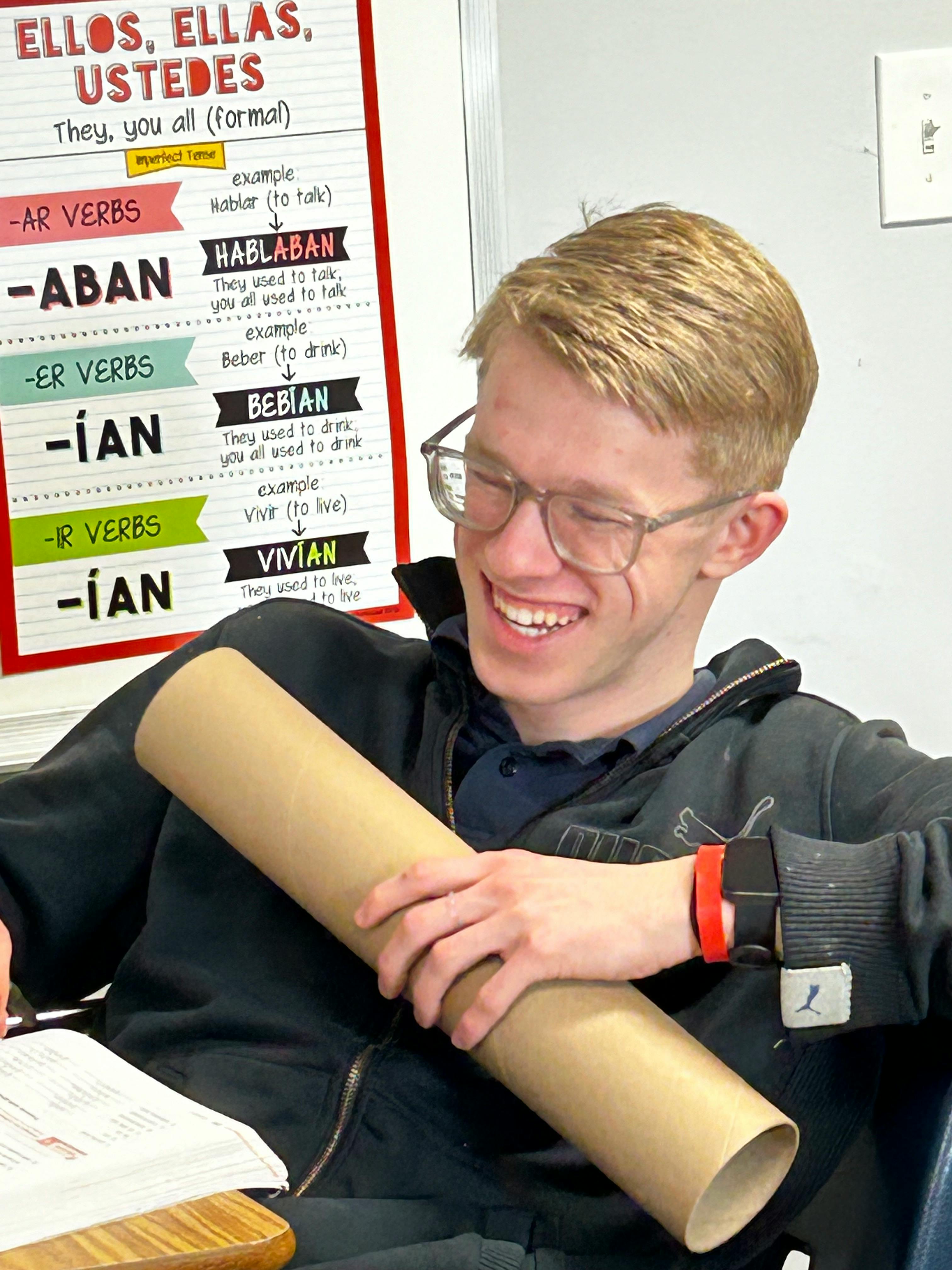 Teen in glasses holding a cardboard tube in a classroom