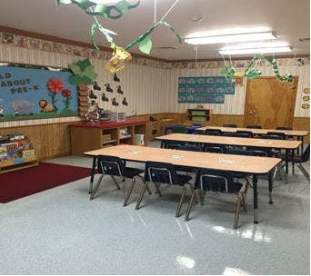 Classroom with small tables and chairs, bulletin board with text