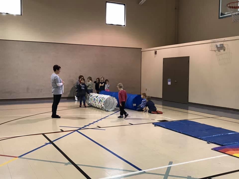 People and children in a gym with tunnels and mats