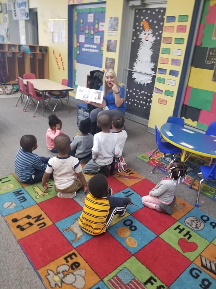 Person reading a book to a group of children in a classroom