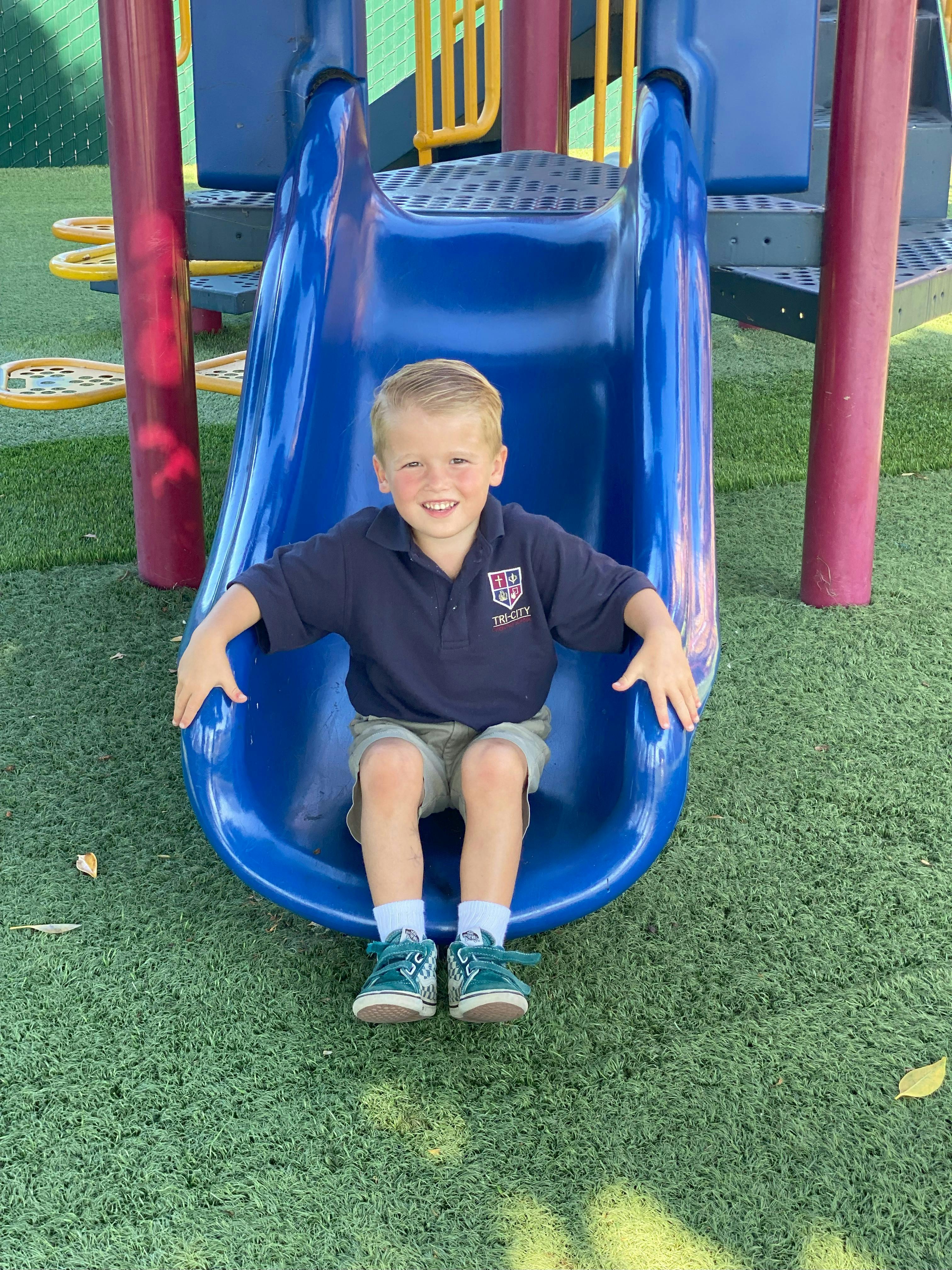 Child sitting at the bottom of a blue slide on a playground