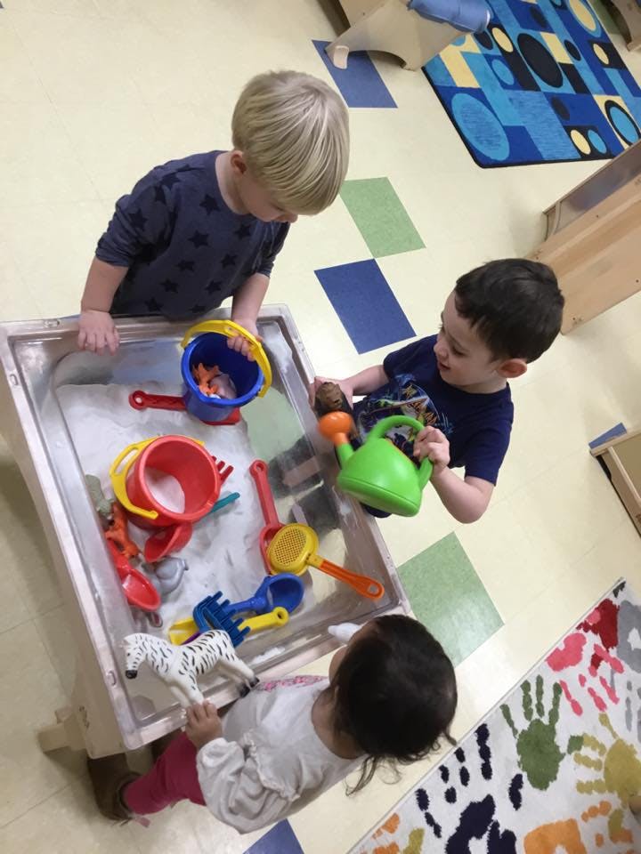 Three children playing with toys in a sand table
