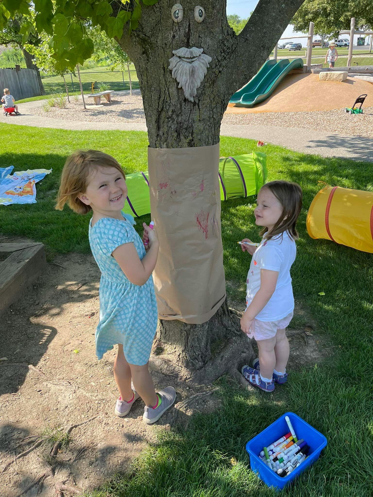 Two children decorating a tree with a face on it