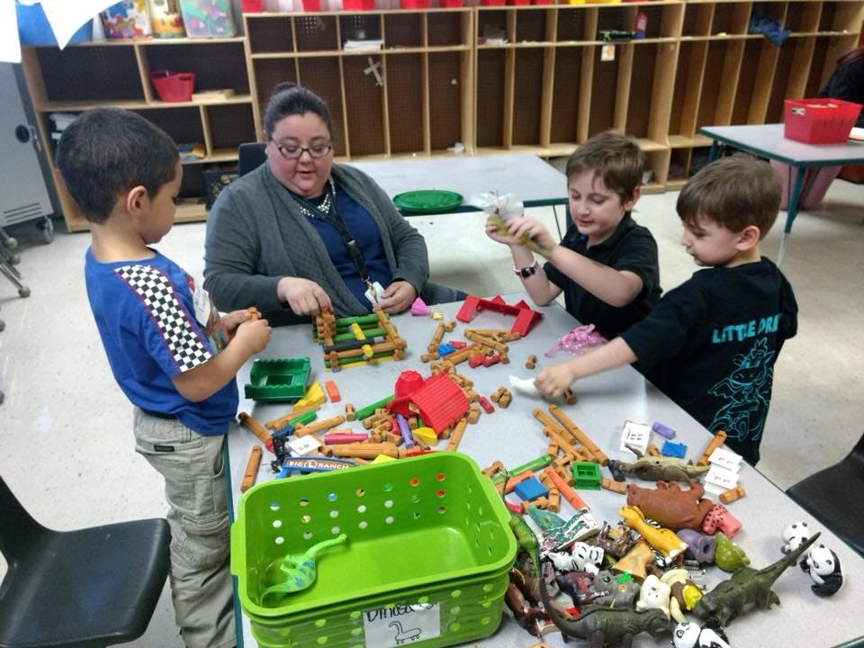 Adult and three children playing with toys at a table in a classroom