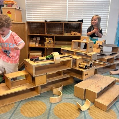 Children playing with wooden blocks and toy vehicles in a classroom