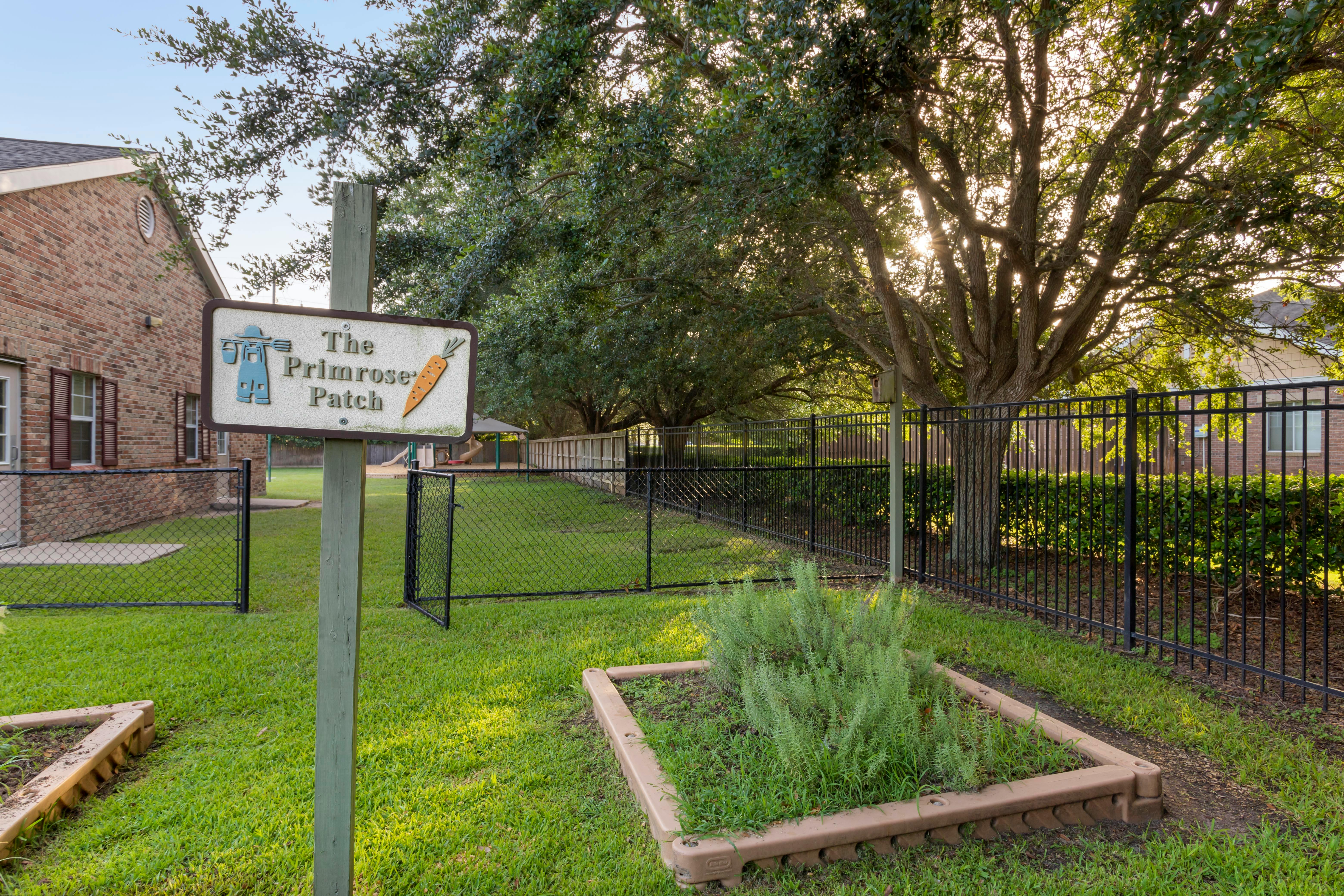A sign that reads "The Primrose Patch" with a small garden bed in front of it