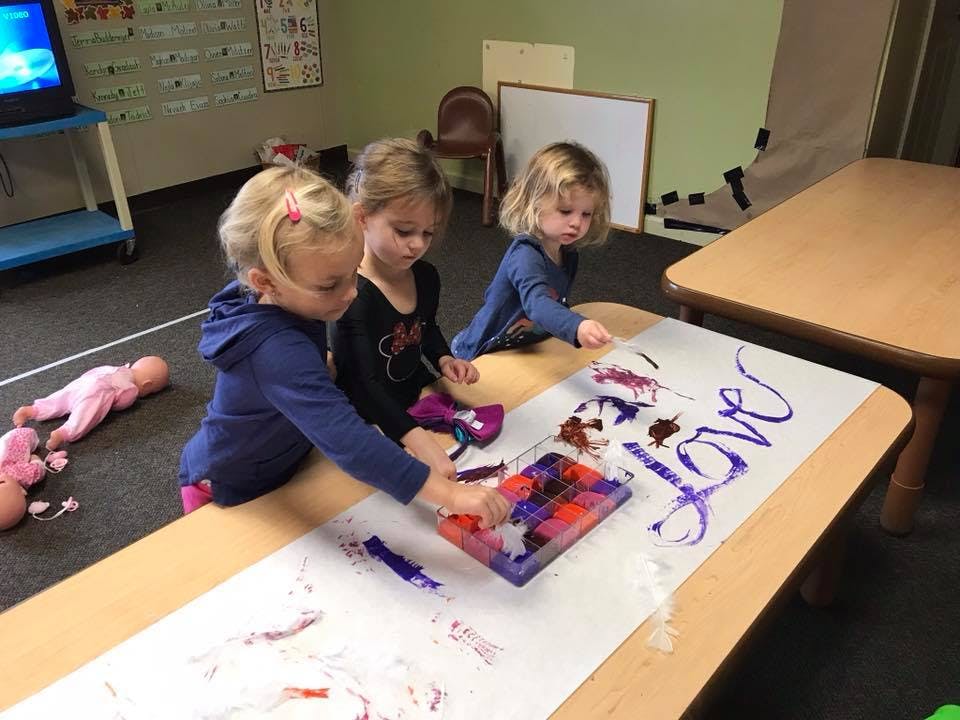 Three children painting on a long sheet of paper