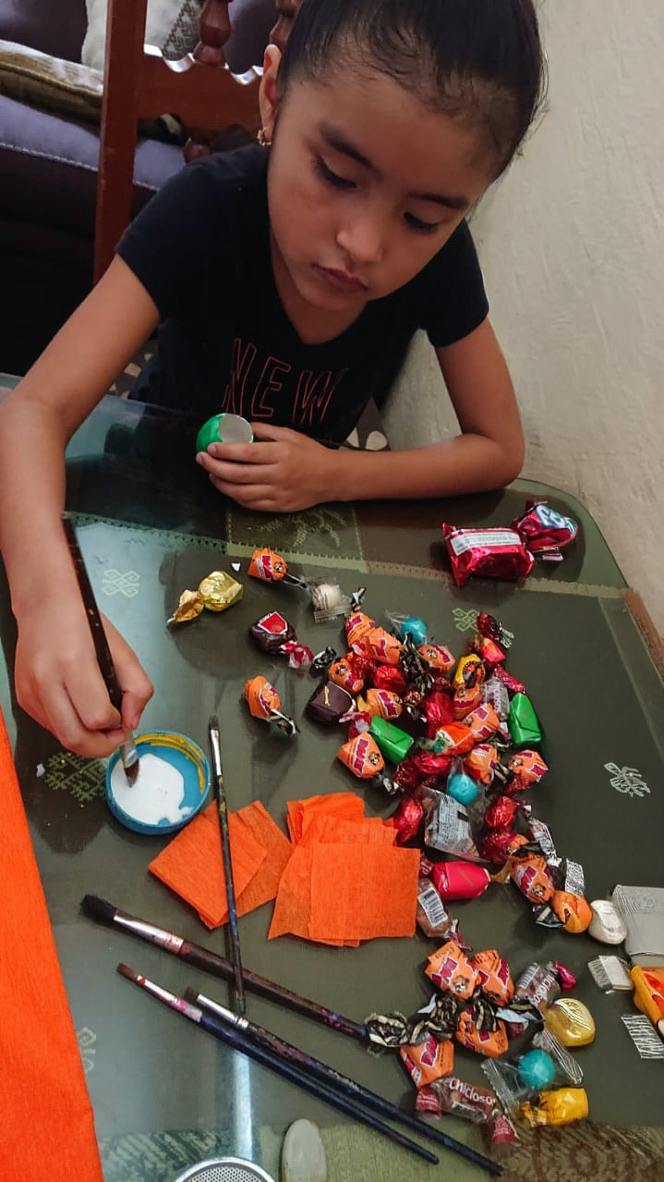Child crafting with paint and brushes on a table scattered with candy wrappers
