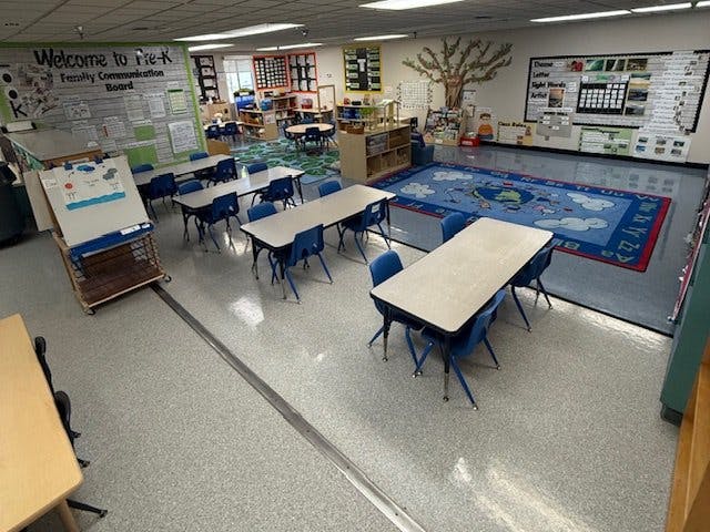 Empty preschool classroom with tables, chairs, and a colorful rug
