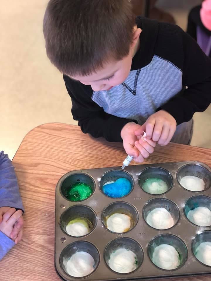 Child using a dropper to add liquid to a muffin tin with colored substances