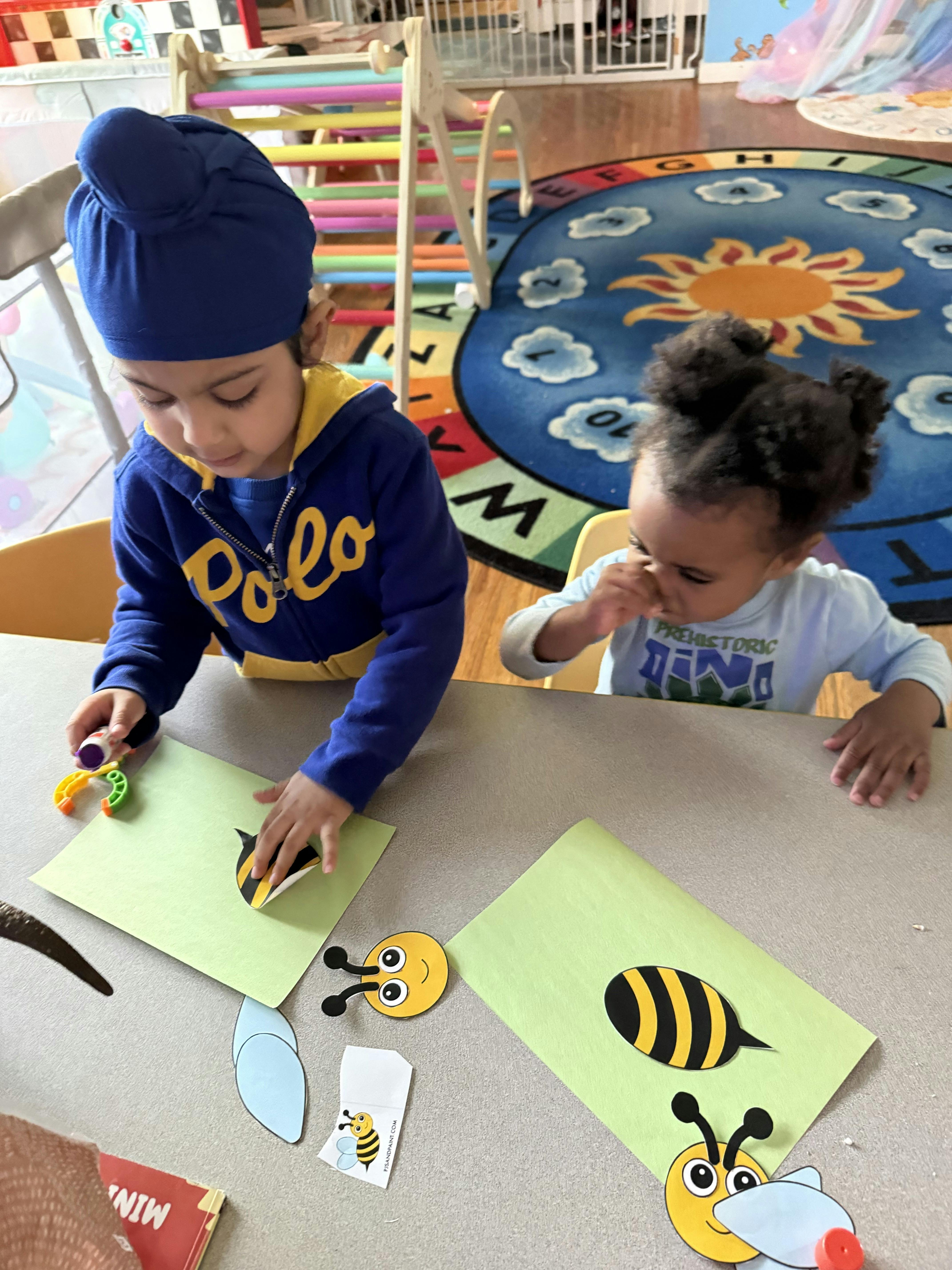 Two children sitting at a table crafting paper bee cutouts