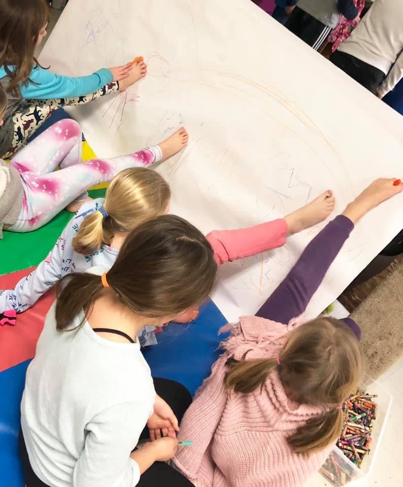 Children drawing on a large sheet of paper on the floor