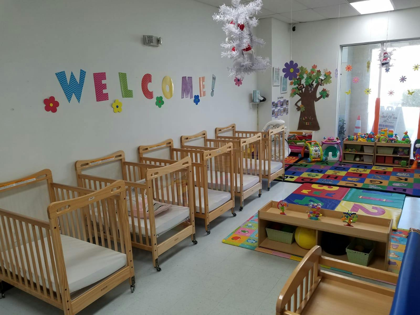 Row of wooden cribs in a room with a colorful rug and wall decorations