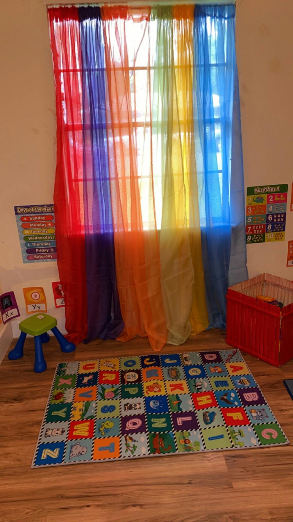Rainbow sheer curtains over a window in a classroom with an alphabet rug