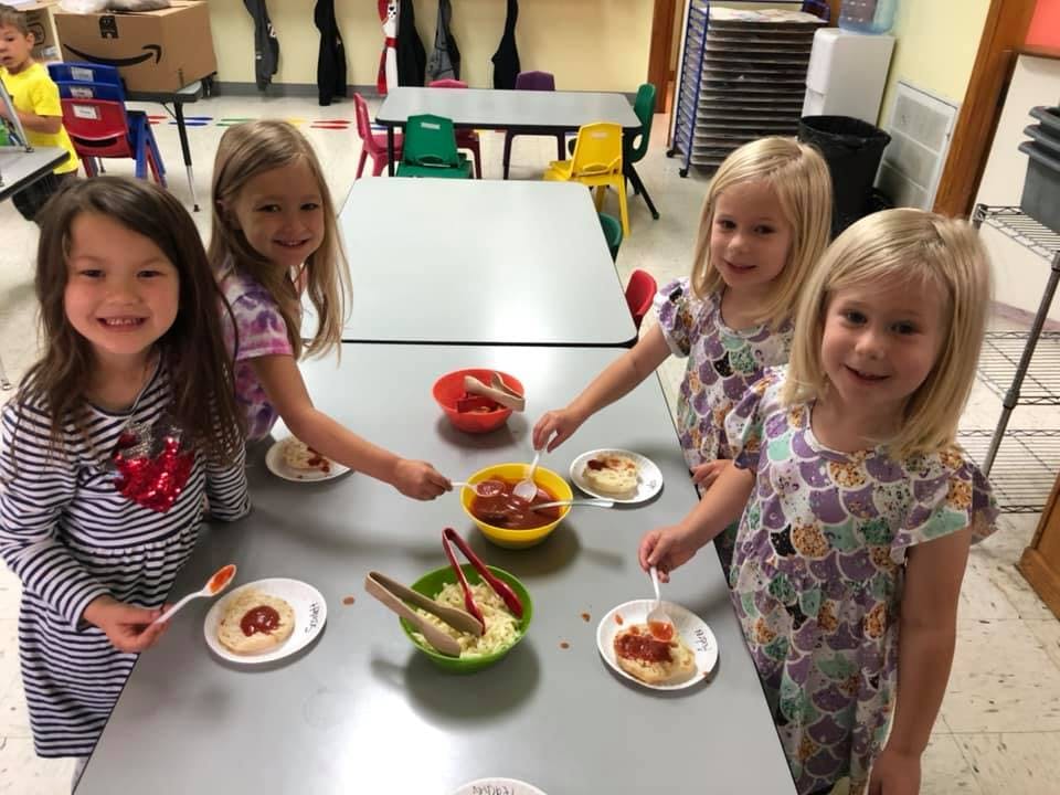 Four children serving themselves food from bowls on a table