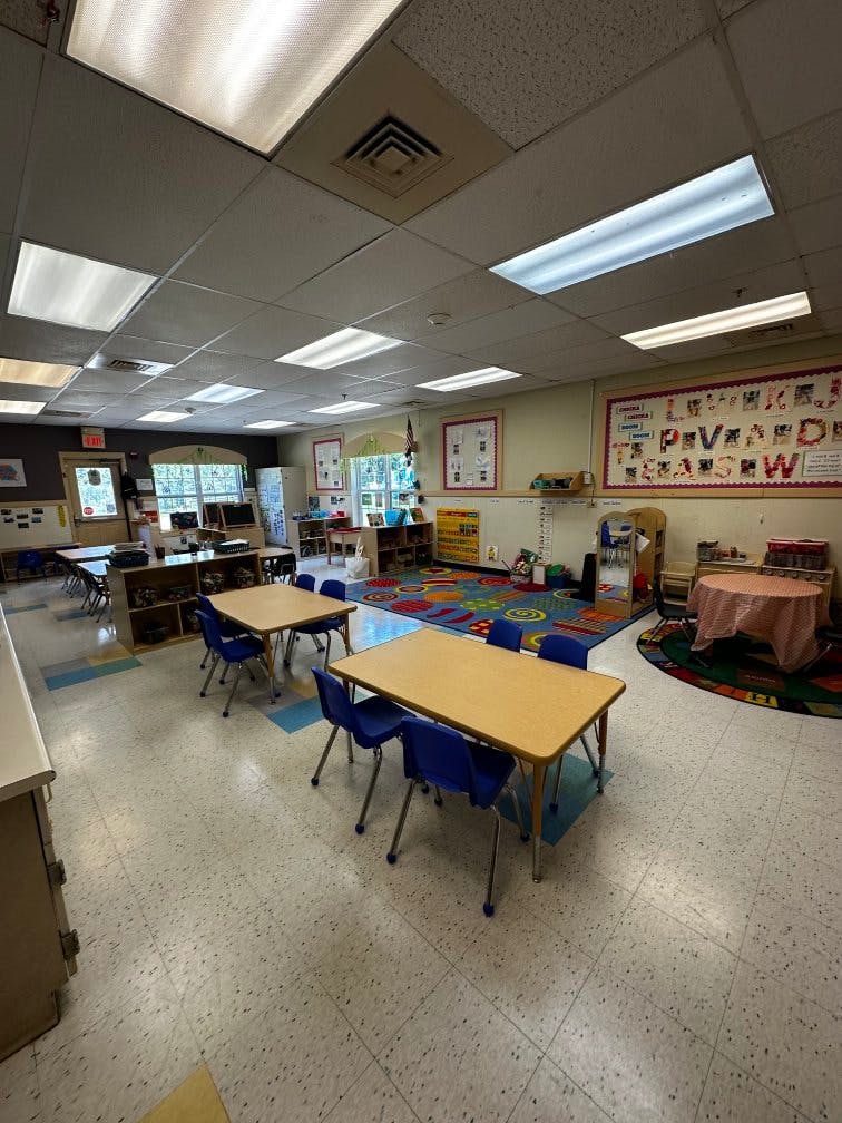 Empty classroom with small tables, blue chairs, and a colorful rug