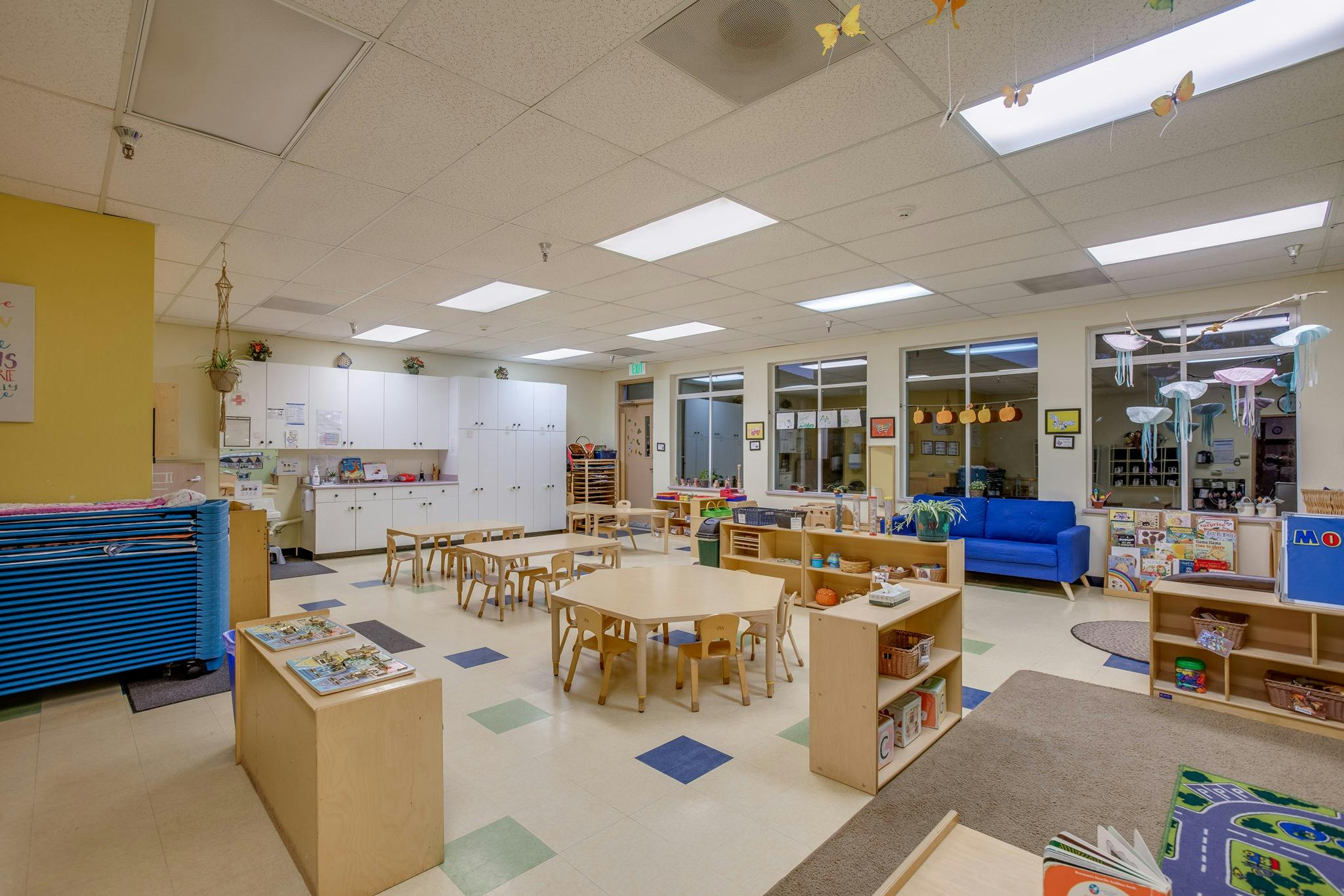 Classroom with small tables and chairs, shelves with books and toys