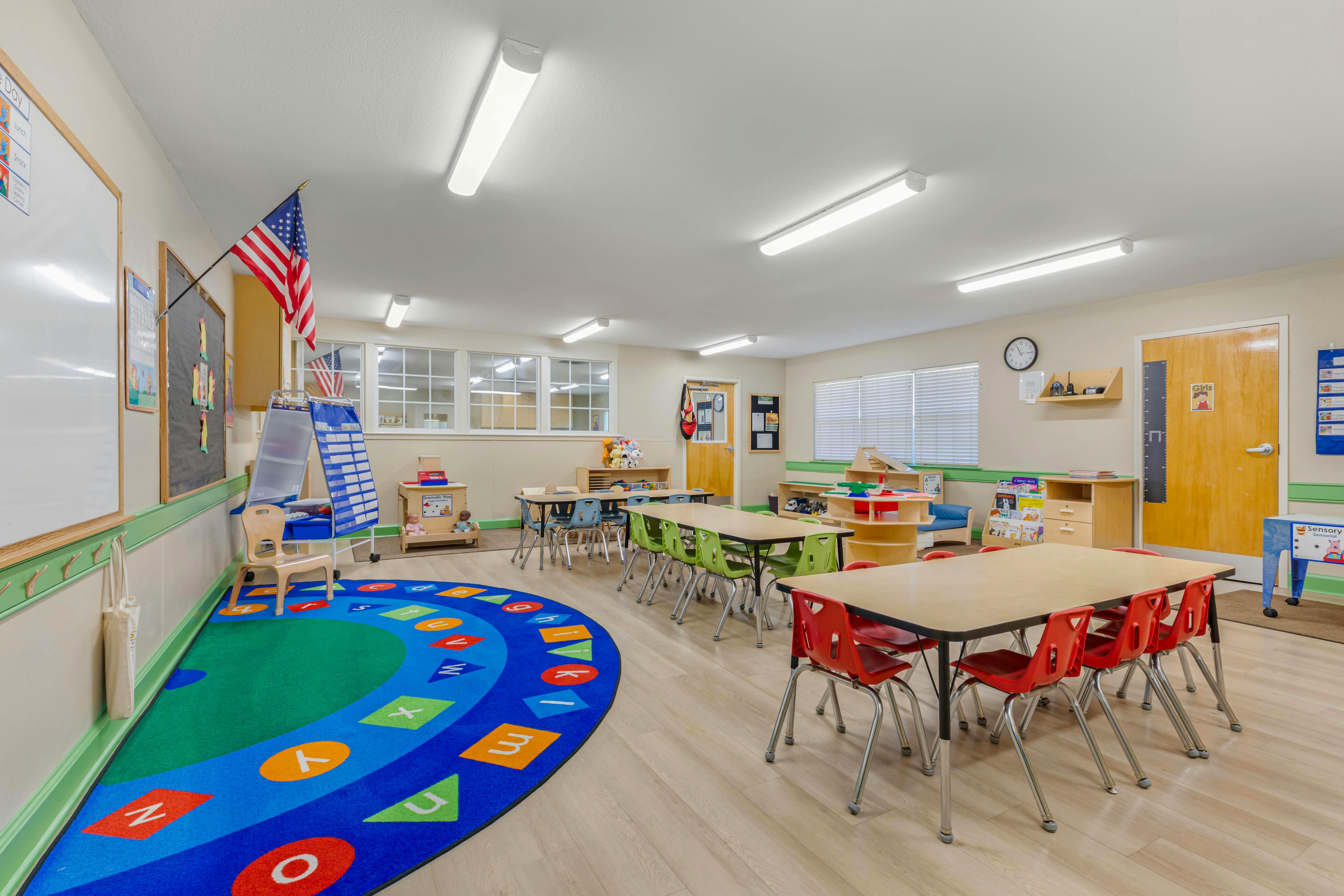 Classroom with tables, chairs, a colorful alphabet rug, and learning materials