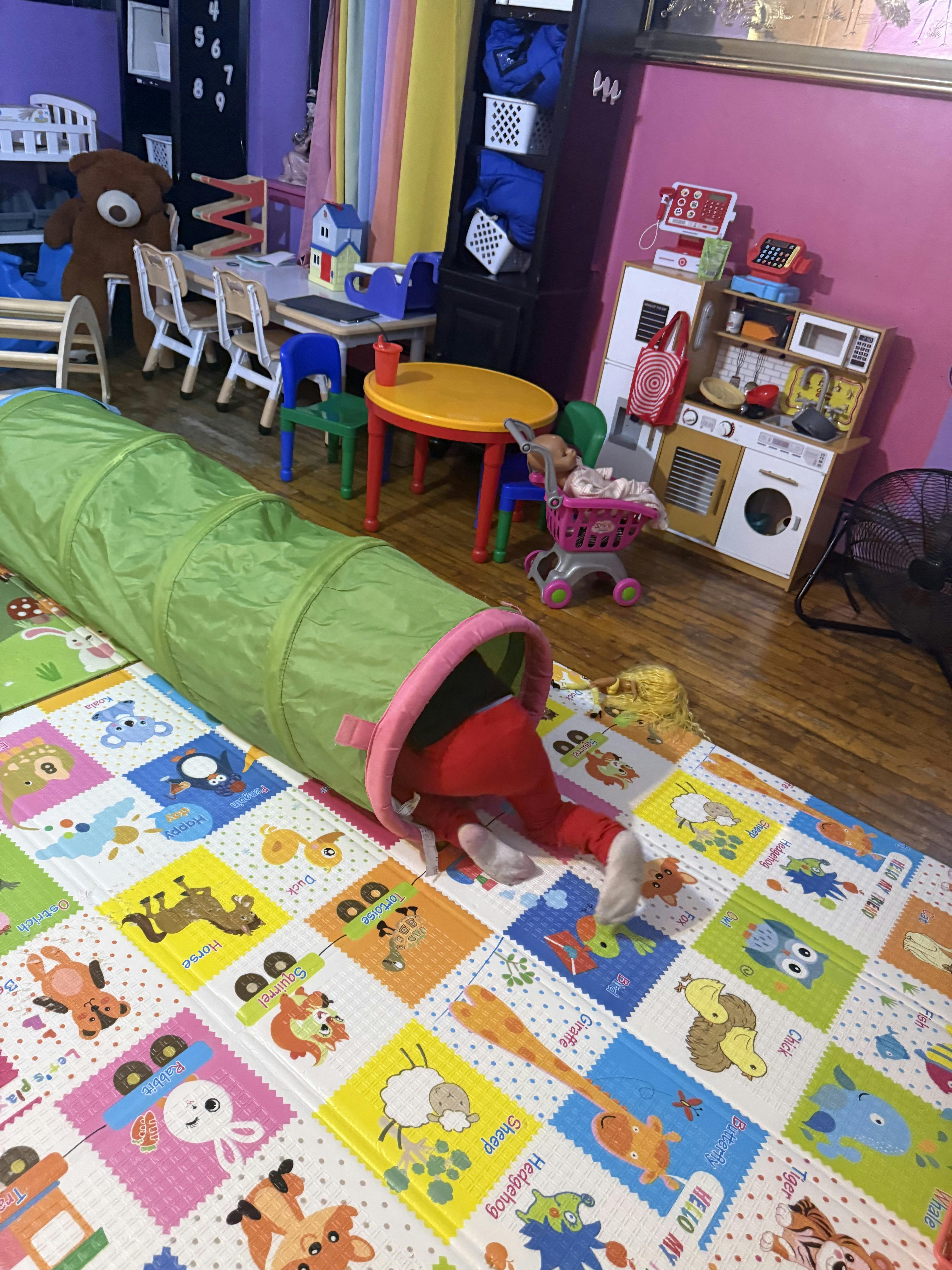 Child crawling through a green play tunnel on a colorful mat
