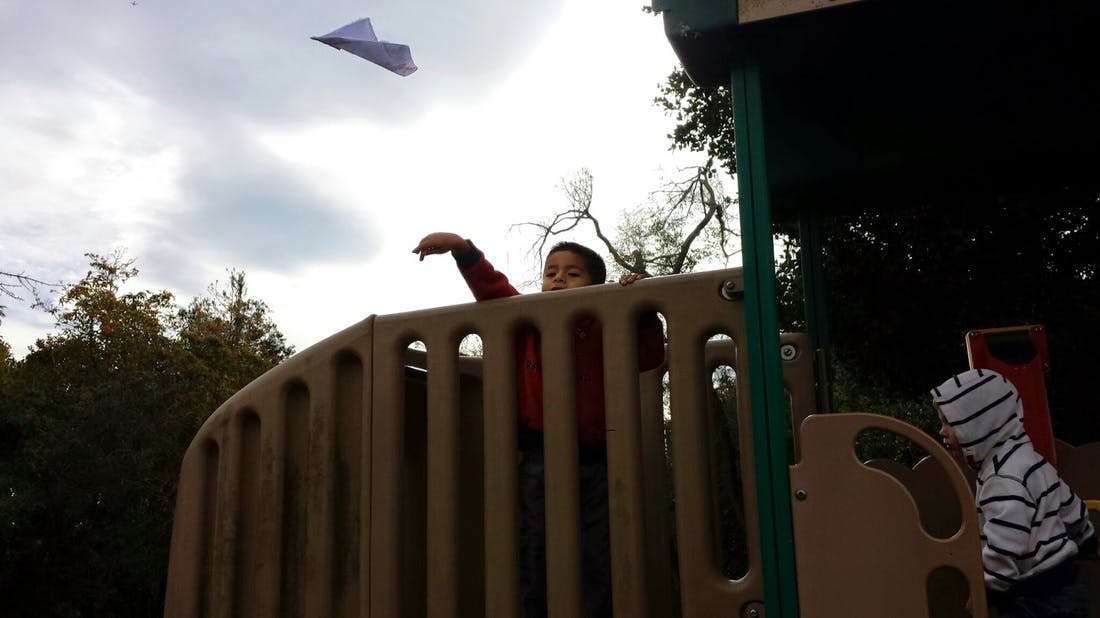 Child throwing a paper airplane from a playground structure
