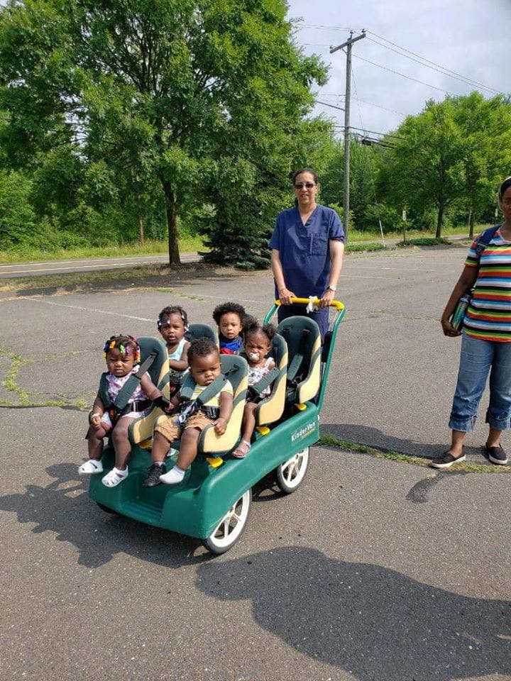 Person pushing a multi-child stroller with five children seated inside