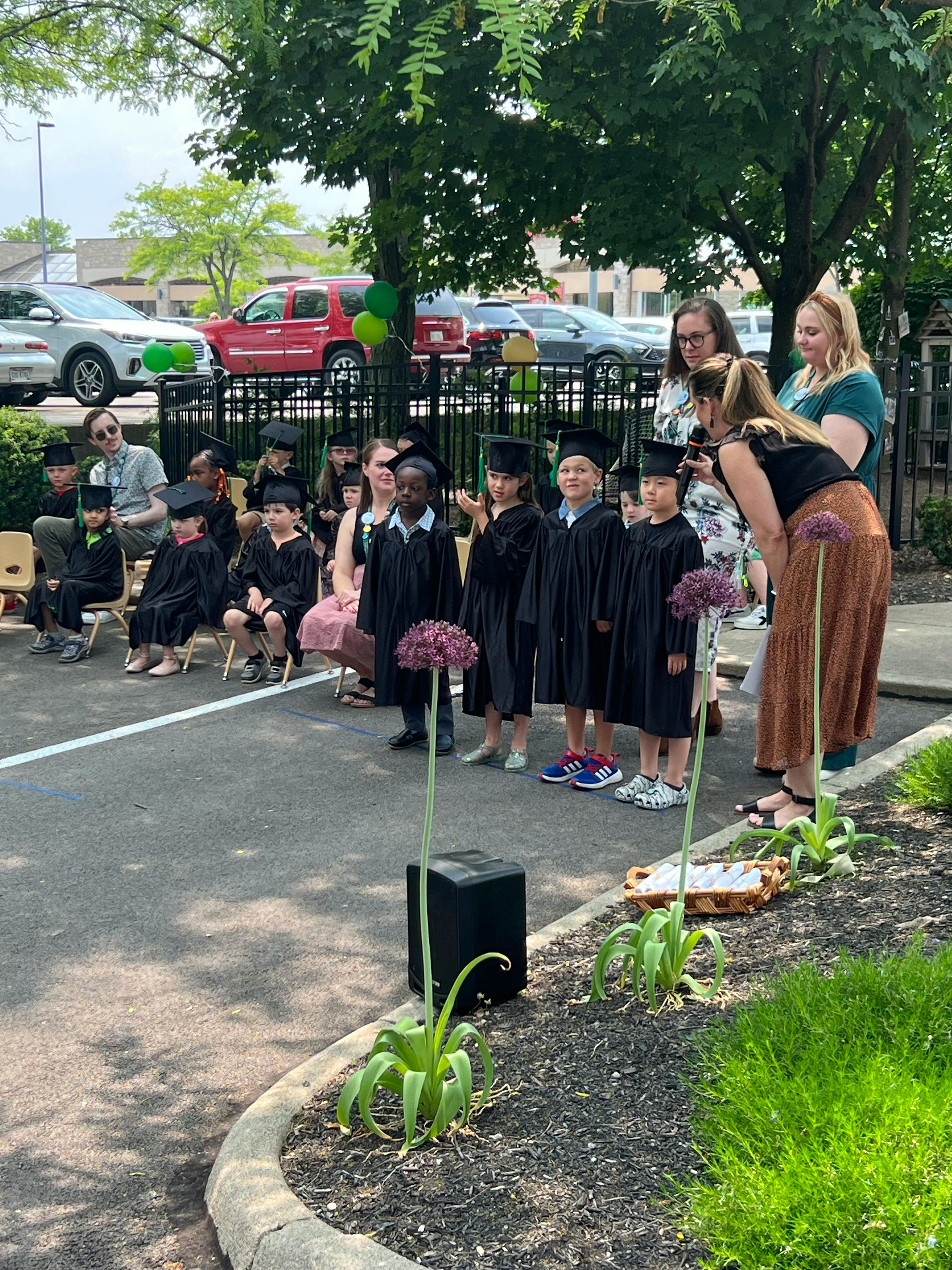Children in graduation caps and gowns with adults outdoors