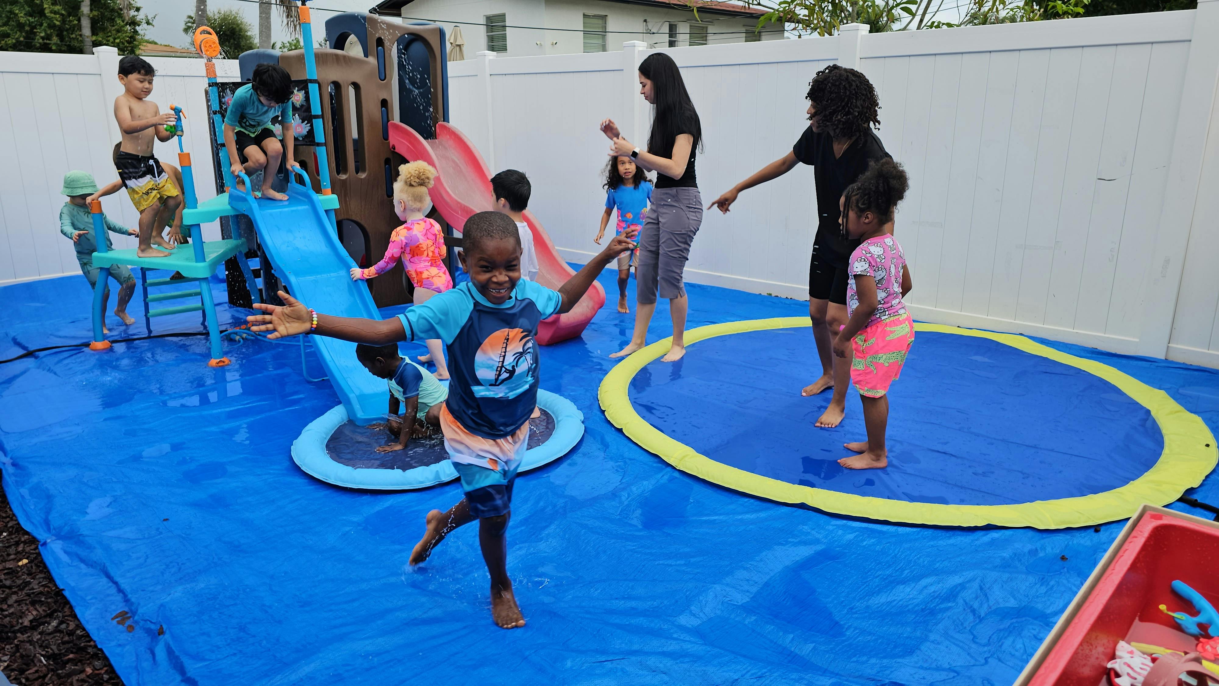Group of children playing on a water slide and splash pad in a backyard