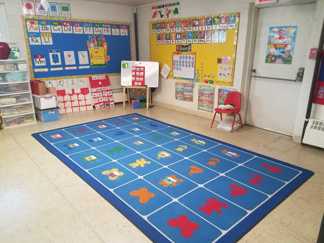 Classroom with a blue rug with colorful shapes, bulletin boards, and a whiteboard