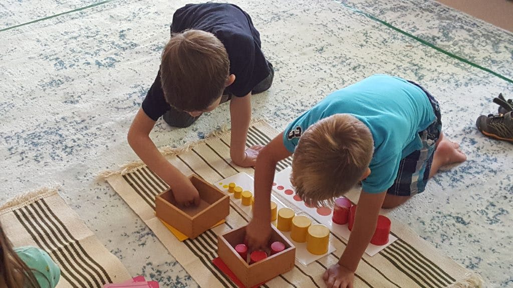 Two children kneeling on a rug playing with wooden blocks and plastic blocks