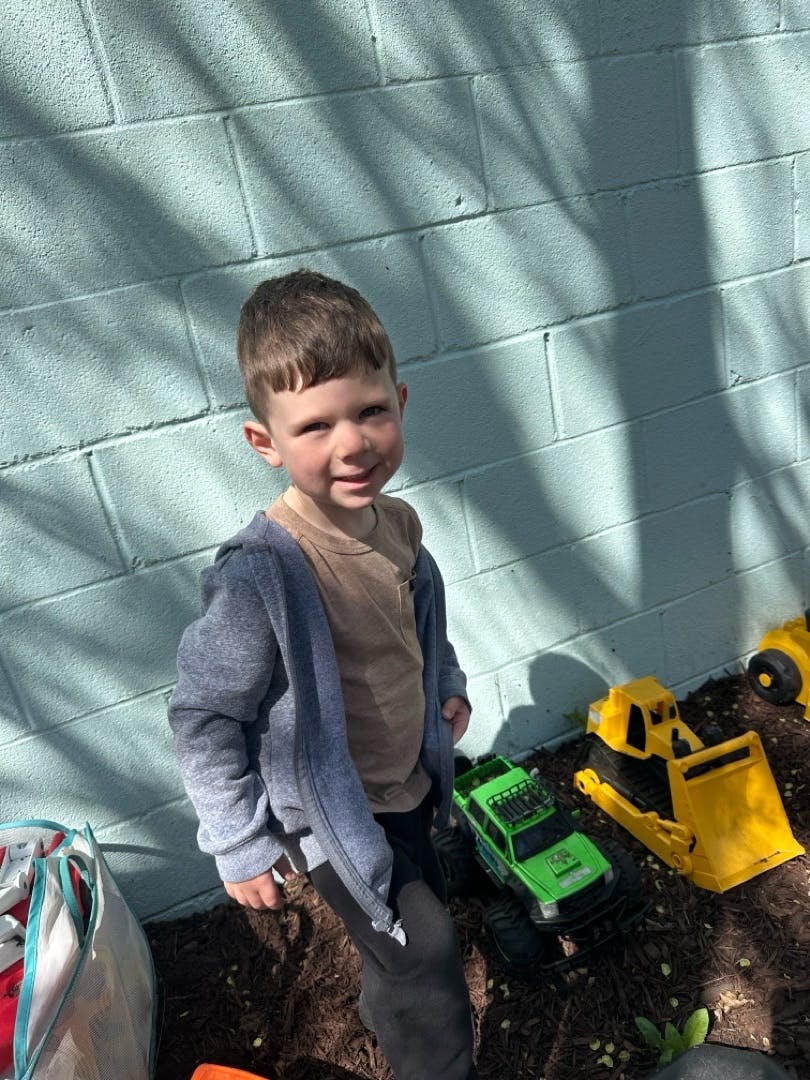 Child standing near toy trucks against a light blue wall