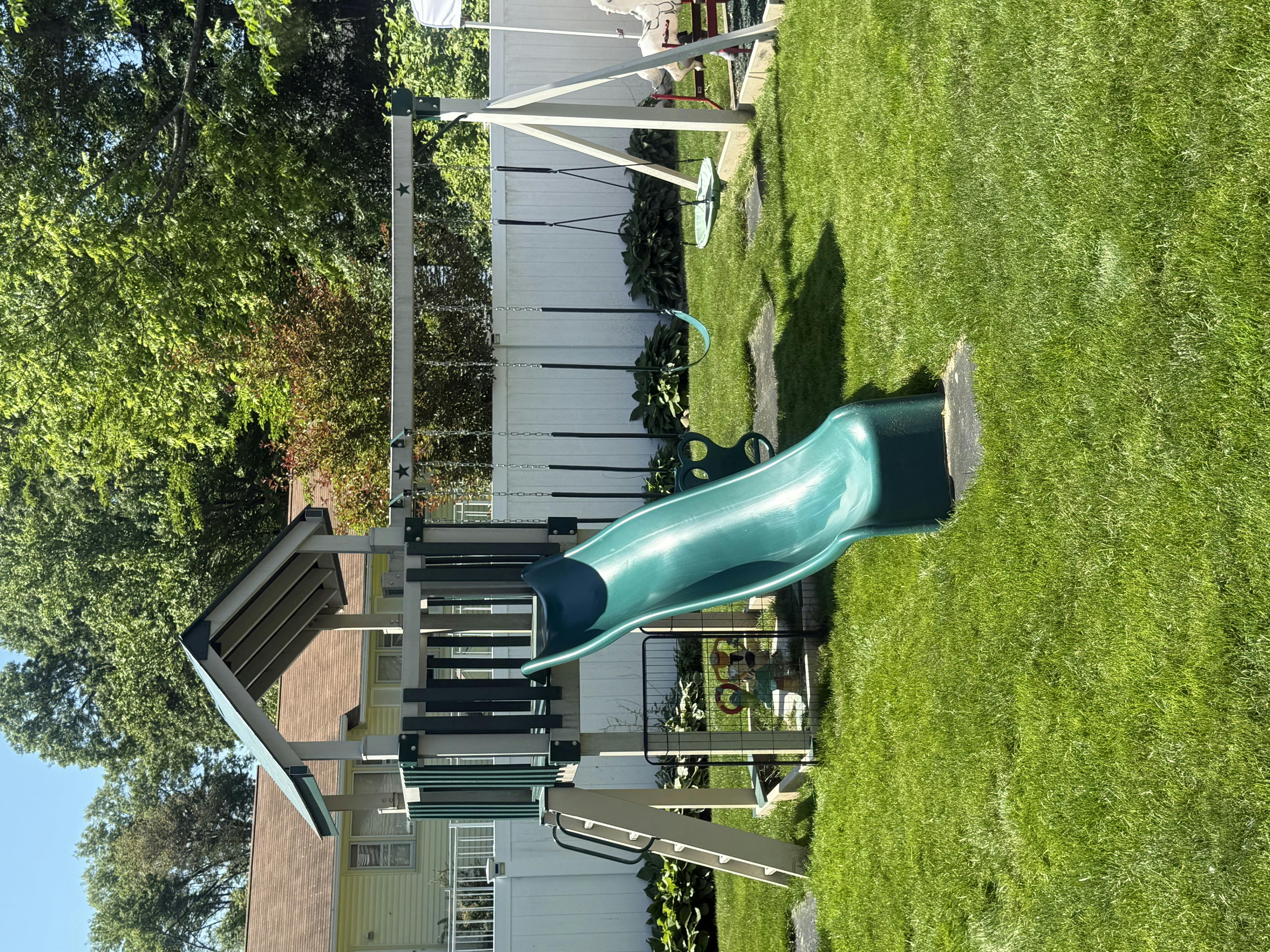 Playground set with a green slide and swings in a grassy yard