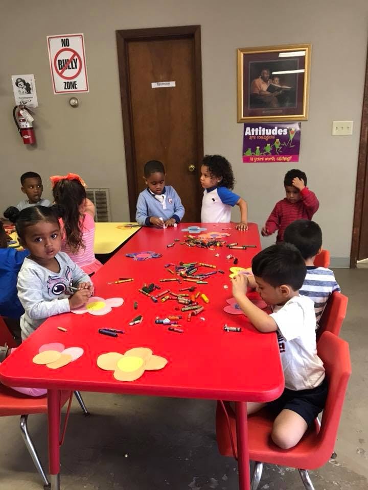 Children sitting at a red table with crayons and craft supplies
