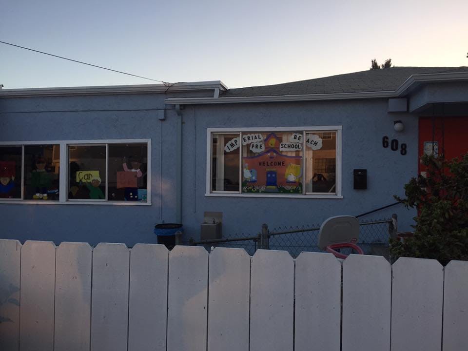 Blue building with windows displaying colorful decorations behind a white fence