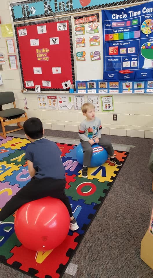 Two children sitting on bouncy balls in a classroom