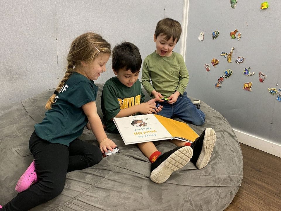 Three children sitting on a beanbag chair reading a book together