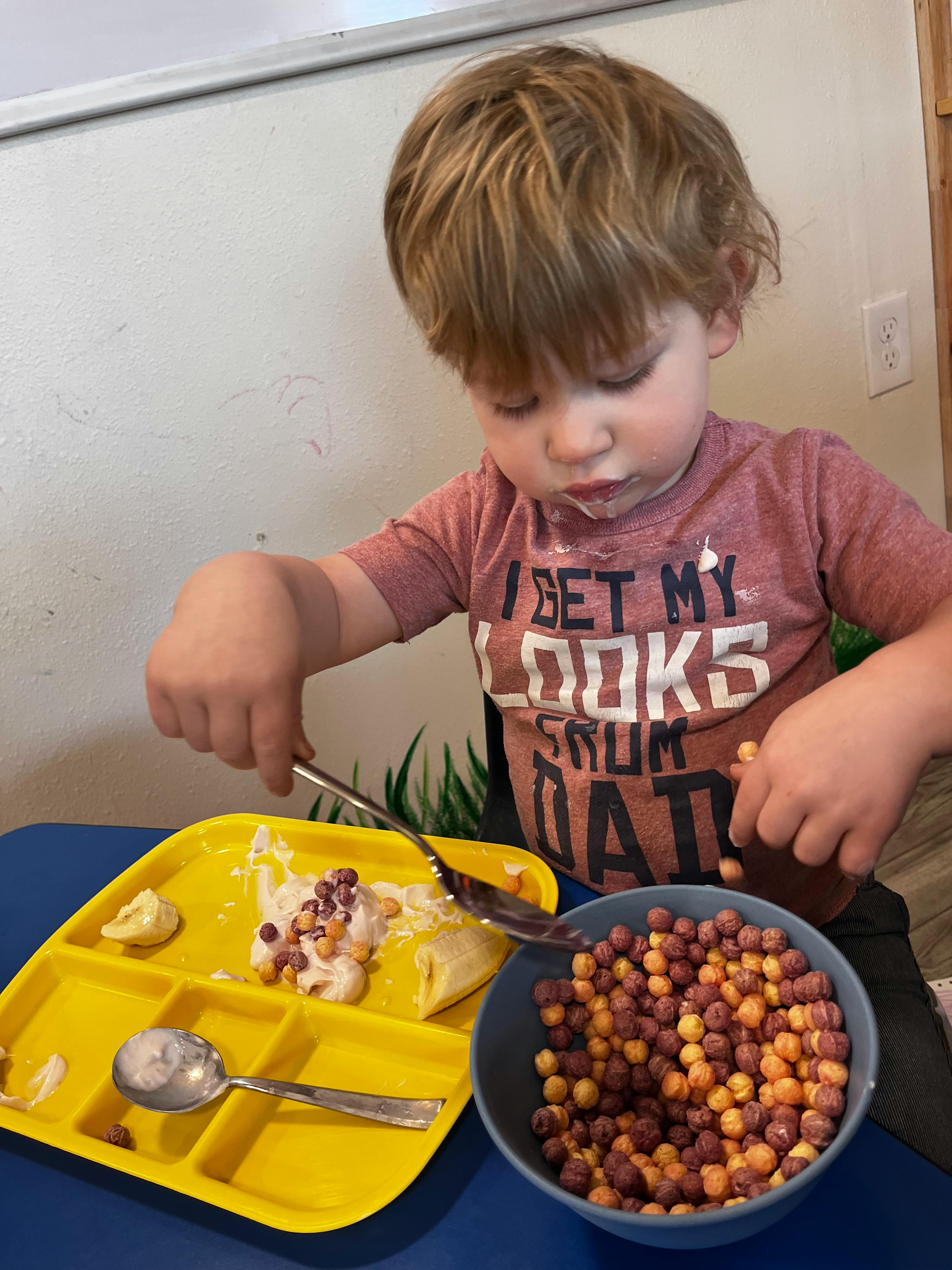 Child eating from a yellow divided plate with a bowl of cereal next to it