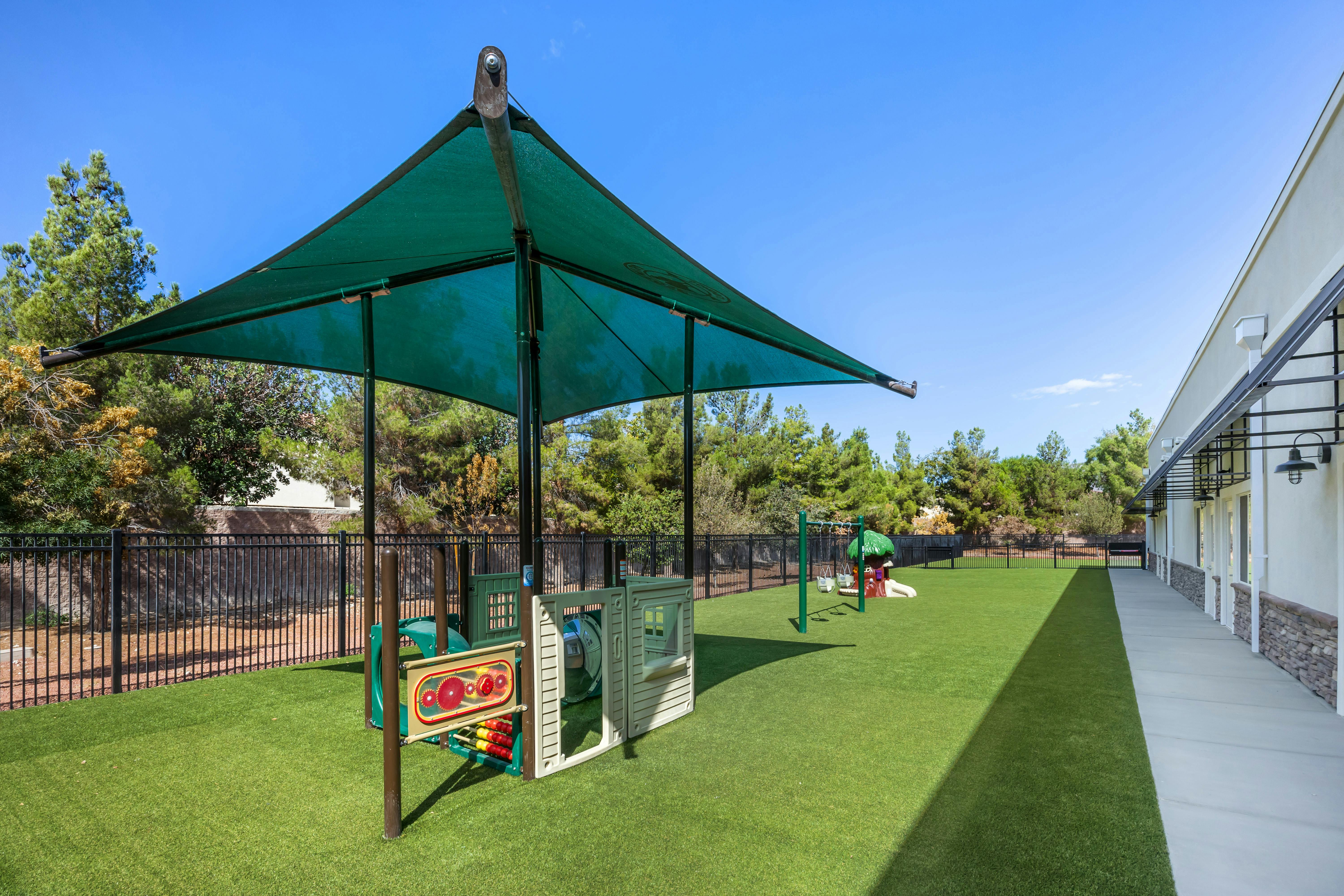 Playground with green turf, shaded structure, swings, and a small slide