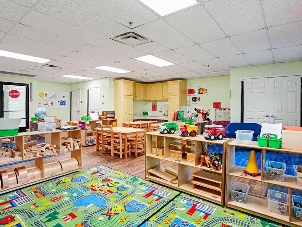 Empty preschool classroom with toys, small tables and chairs, and a playmat